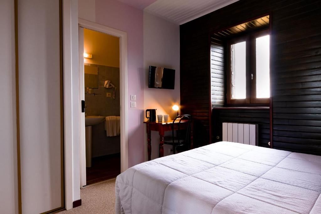 Un dormitorio con cama, escritorio con silla, ventana y baño visible a través de una puerta abierta.