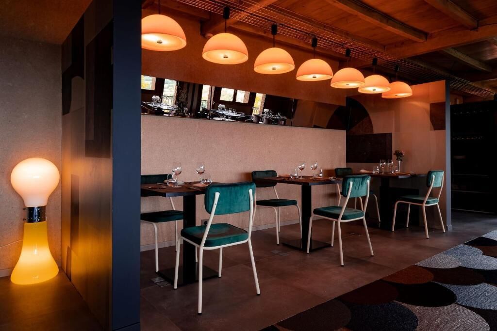 A restaurant with a modern interior, featuring wooden beams, pendant lighting, and green upholstered chairs.