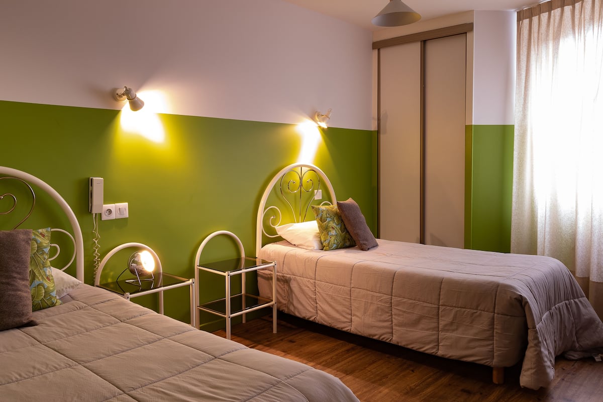 Una habitación con dos camas, una pared de acento verde y un ventanal con cortinas.