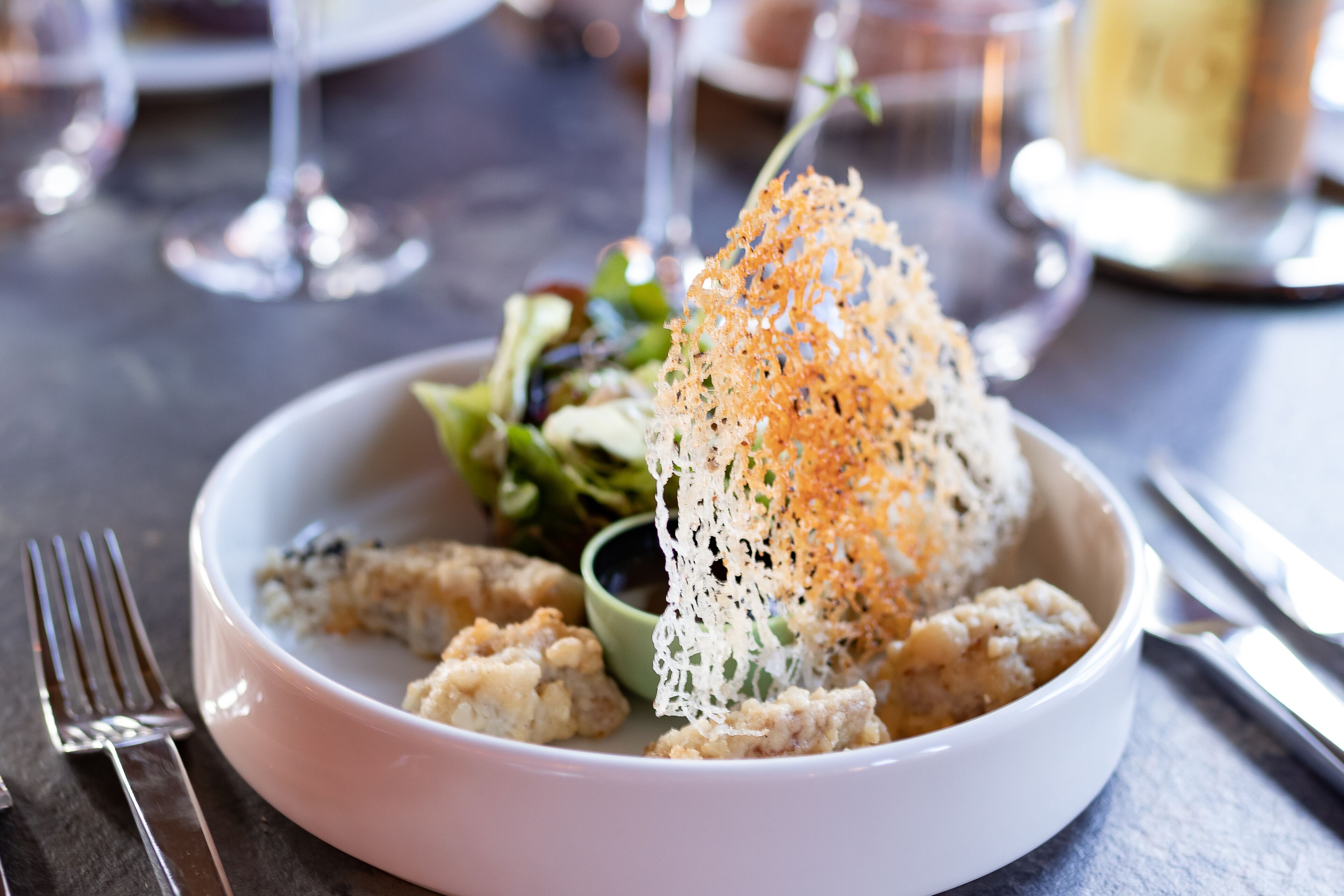 A white bowl with food, including a piece of bread topped with orange garnish, on a table.
