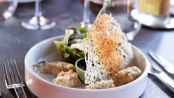 A white bowl with food, including a piece of bread topped with orange garnish, on a table.
