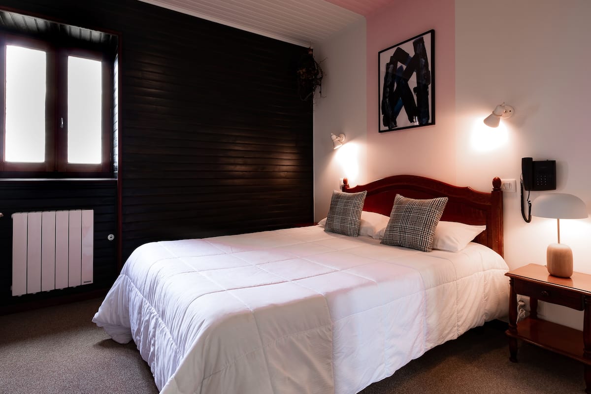 Una cama bien hecha con ropa de cama blanca, un cabecero de madera y dos lámparas de noche.