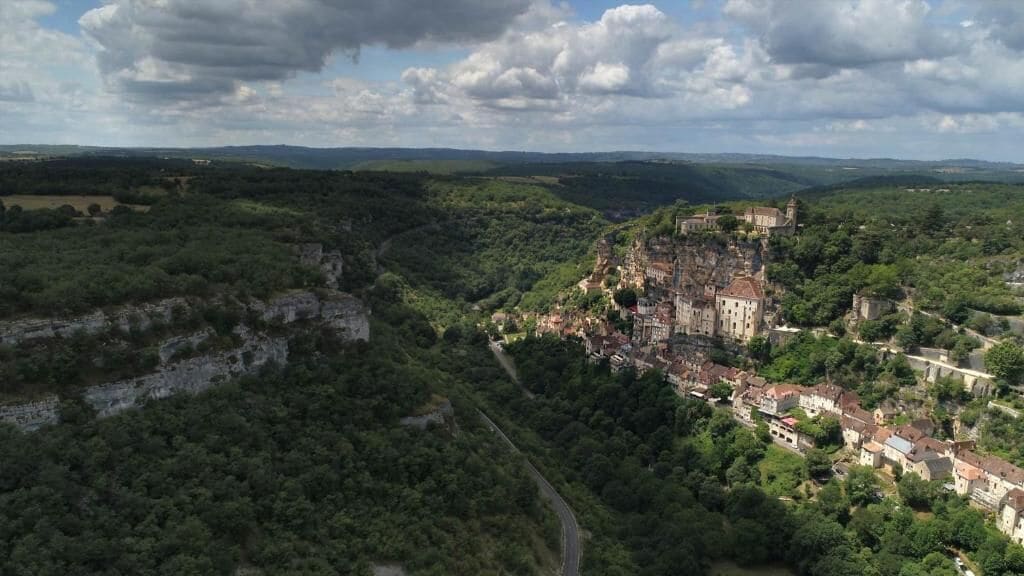 A historic town with a prominent castle, surrounded by lush greenery and a winding road.