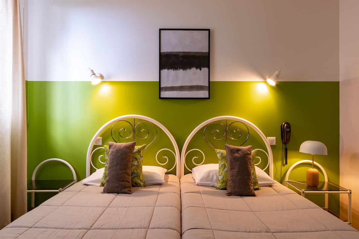 Cama doble con cabecera acolchada, dos almohadas, mesita de noche con lámpara y teléfono en la pared.