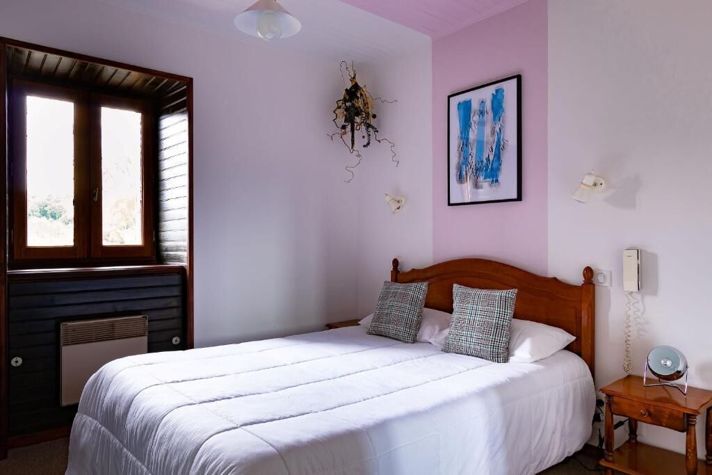 A bedroom with a wooden bed, a radiator, a window, a wall-mounted light, and a framed picture.