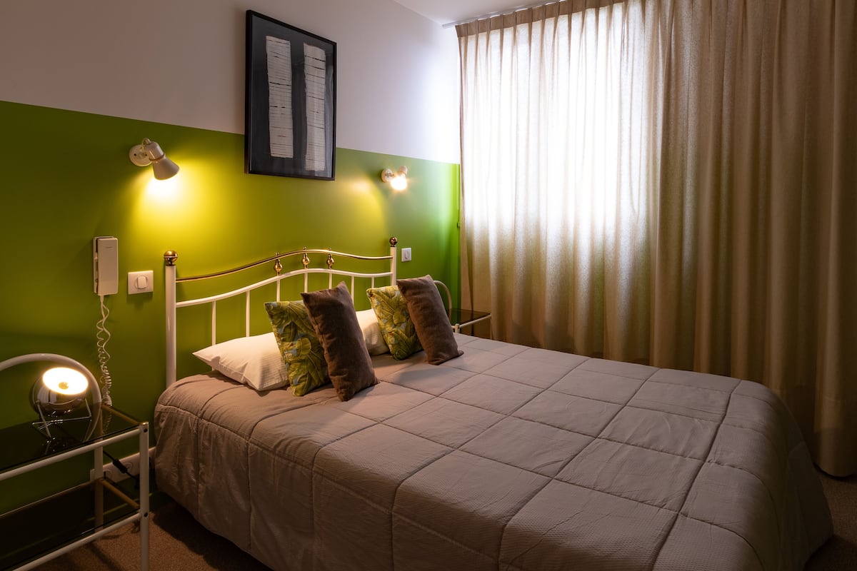 Una cama bien hecha con un edredón color beige, una pared verde y un menú enmarcado encima.