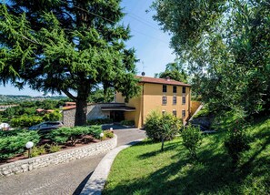 Un edificio giallo con facciata in pietra, circondato da vegetazione lussureggiante e un vialetto in pietra che conduce all'ingresso.