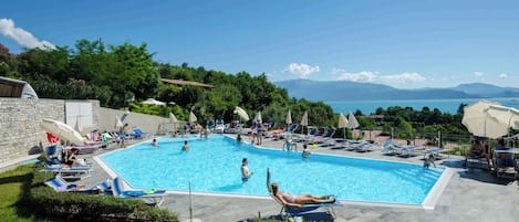 A swimming pool with lounge chairs and umbrellas, surrounded by greenery and a view of the sea.