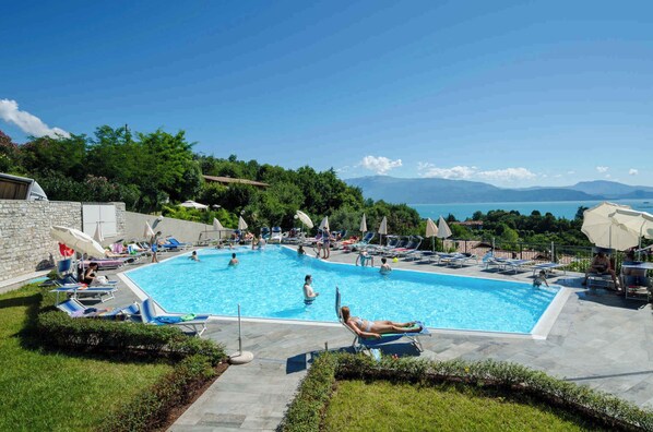 A swimming pool with lounge chairs and umbrellas, surrounded by greenery and a view of the sea.
