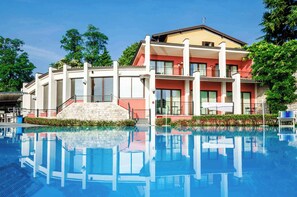 A hotel with a swimming pool, a staircase leading to the entrance, and a balcony with outdoor furniture.