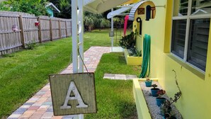 Un patio trasero con valla de madera, un sendero pavimentado y un edificio amarillo con una ventana.