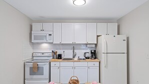 Una cocina compacta con gabinetes blancos, microondas, estufa, refrigerador y cafetera.