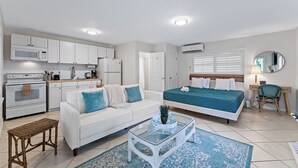 Un apartamento moderno con kitchenette, un sofá blanco, una cama con ropa de cama color turquesa y un pequeño comedor.
