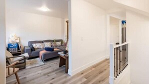 Amplia sala de estar con sofá gris, piso de madera y escalera con barandilla blanca.