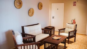 A room with a white sofa, two wooden chairs, and a small wooden table. There are three wooden wall decorations and a fire extinguisher mounted on the wall. - EntreOlivos (Badajoz)