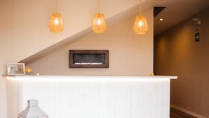 A reception area with a white reception desk, three pendant lights, a framed picture, and a wall-mounted screen. - EntreOlivos (Badajoz)