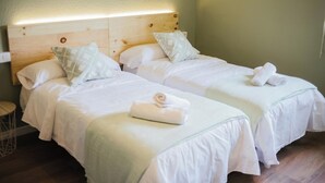 Two single beds with wooden headboards, white bedding, and a small round table. - EntreOlivos (Badajoz)