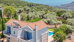 Eine moderne Villa mit Swimmingpool, umgeben von üppiger Vegetation und Blick aufs Meer.