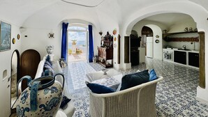 A spacious living area with a view to the sea, a kitchen, and a dining area with blue and white patterned tiles. - YourHome - Assia House Praiano (Praiano)