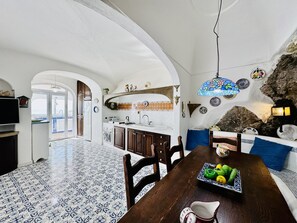 A spacious kitchen with an open layout, a dining area with a table set for two, and a view of the sea through an archway. - YourHome - Assia House Praiano (Praiano)
