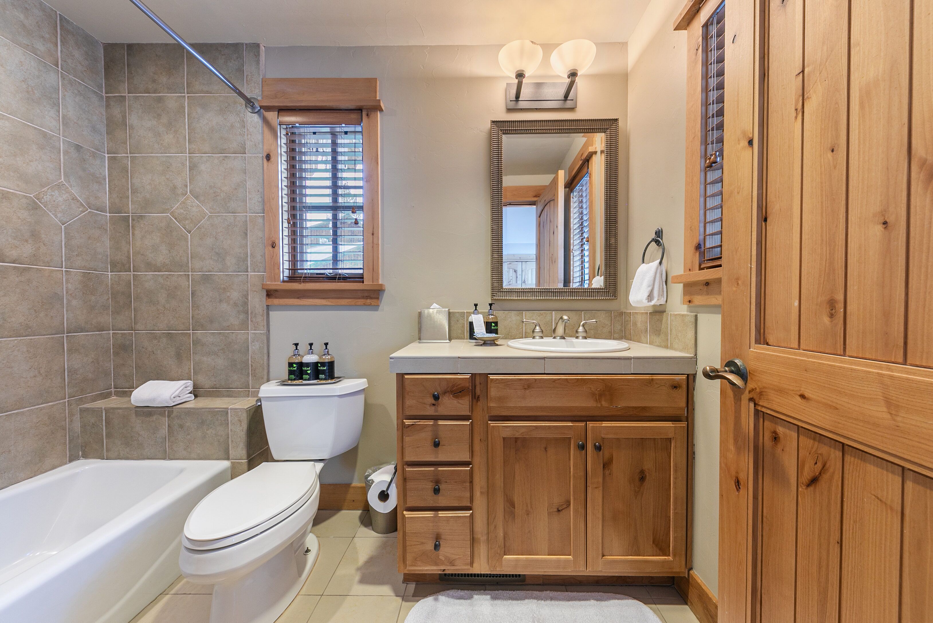 A bathroom with a bathtub, toilet, wooden vanity, and a large mirror.