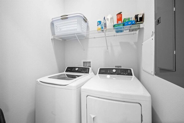 Een wasserette met twee wasmachines, een droogrek en een plank met diverse wasmiddelen.