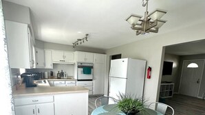 A modern kitchen with white cabinets, a central island, and a dining area with a round table and chairs. - Spacious 3BR Ranch w/ Hot Tub & Yard • Near Kings Island (Mason)