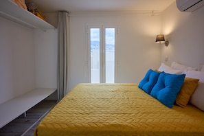 A room with a bed, a bench, a window, and an air conditioning unit.