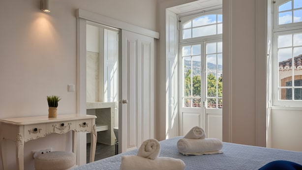 Une chambre à coucher avec un lit, deux serviettes, une table de chevet, un miroir et une fenêtre donnant sur la ville.