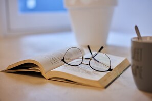 An open book with glasses on top, a coffee cup, and a spoon.