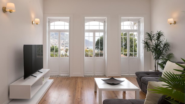 A modern living room with a flat-screen TV, white furniture, and large windows offering a view of the outdoors. - Luna Rossa - Artcooking by Homie (Funchal)