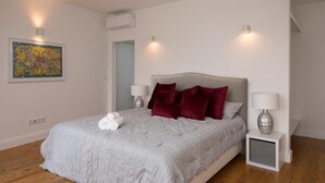 A neatly arranged bedroom with a bed, two bedside lamps, and a wall-mounted air conditioner. - Luna Rossa - Artcooking by Homie (Funchal)