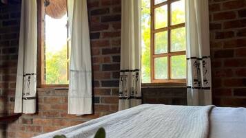 Relax in this serene space with a view of lush greenery through the large window, accompanied by a comfortable bed and a natural touch from the potted plant.