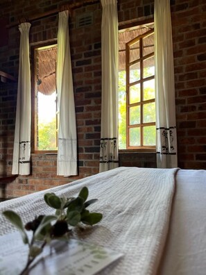A room with a brick wall, a window with curtains, and a bed with a white bedspread. - Southern Cross Estate (Bulawayo)