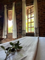 A room with a brick wall, a window with curtains, and a bed with a white bedspread.