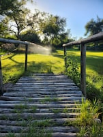 A wooden pathway leading to a grassy area with trees in the background.