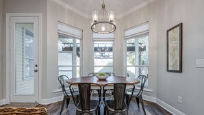A dining room with a wooden table, six chairs, a chandelier, and large windows. - Lei'd Back * Golf Cart Included & Pet Friendly * Salt Water Vacations (Destin)