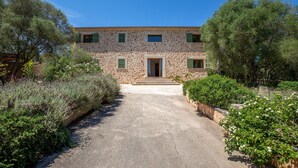 A stone building with a central entrance, surrounded by greenery and a paved path leading to the door. - Camadix, Finca 5StarsHome Mallorca (Costitx)