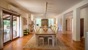 A spacious dining area with a wooden table and chairs, a chandelier, and a view of the outdoors through large sliding glass doors. - Camadix, Finca 5StarsHome Mallorca (Costitx)