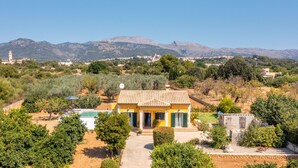 Una villa amarilla con techo de tejas, rodeada de olivos y con una montaña de fondo.