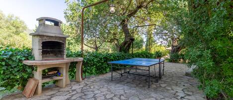 An outdoor patio with a stone floor, a pizza oven, and a ping pong table.