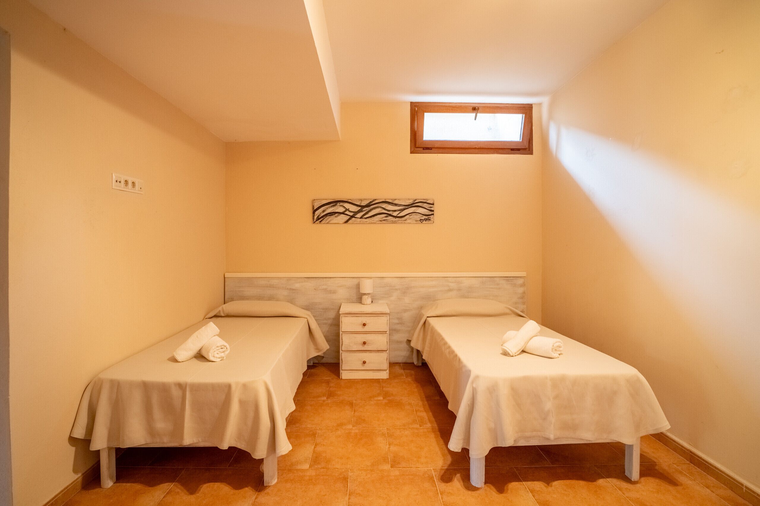 A small, clean room with two single beds, a nightstand, and a wall-mounted artwork.