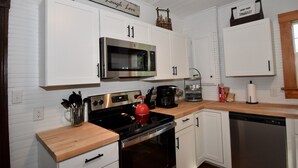 A kitchen with white cabinets, a stainless steel microwave, a red kettle, and a coffee maker. - Peaceful Farmhouse w/ Fire Pit & Updated Comforts (Monroe)