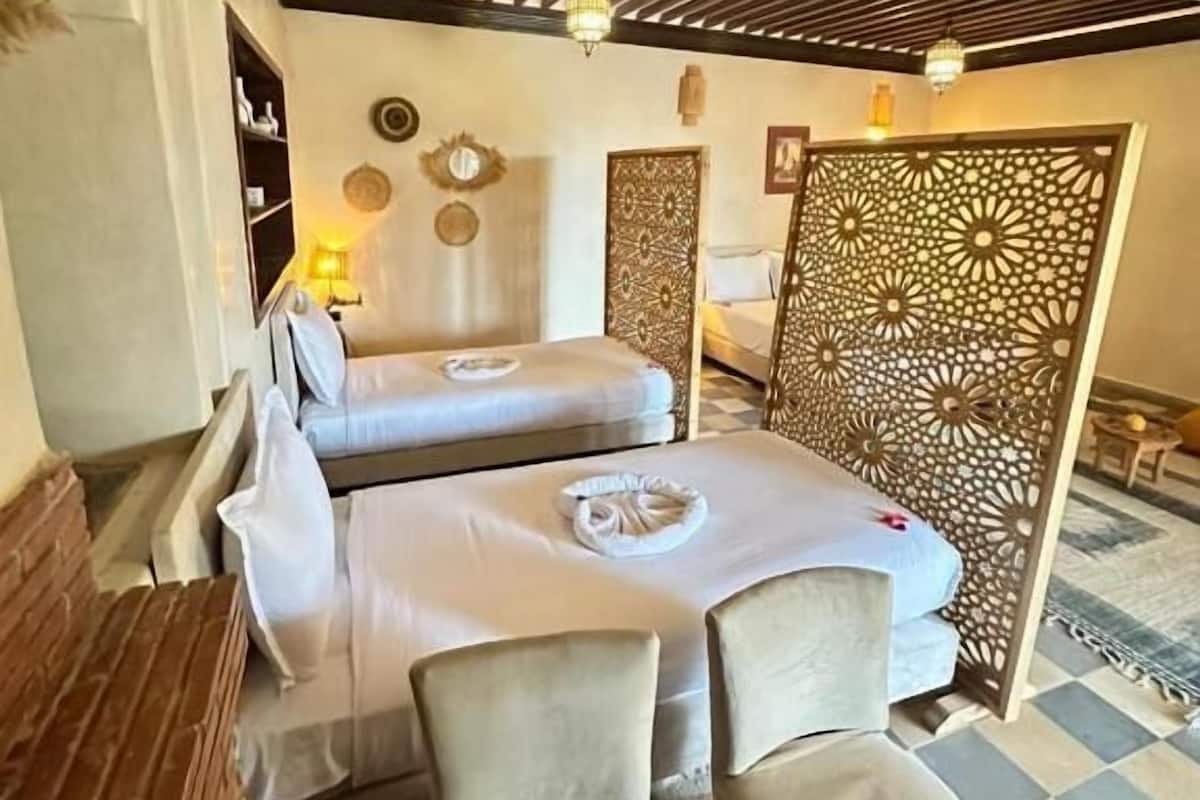 A hotel room with two beds, a wooden desk, a decorative wall panel, and a checkered floor.