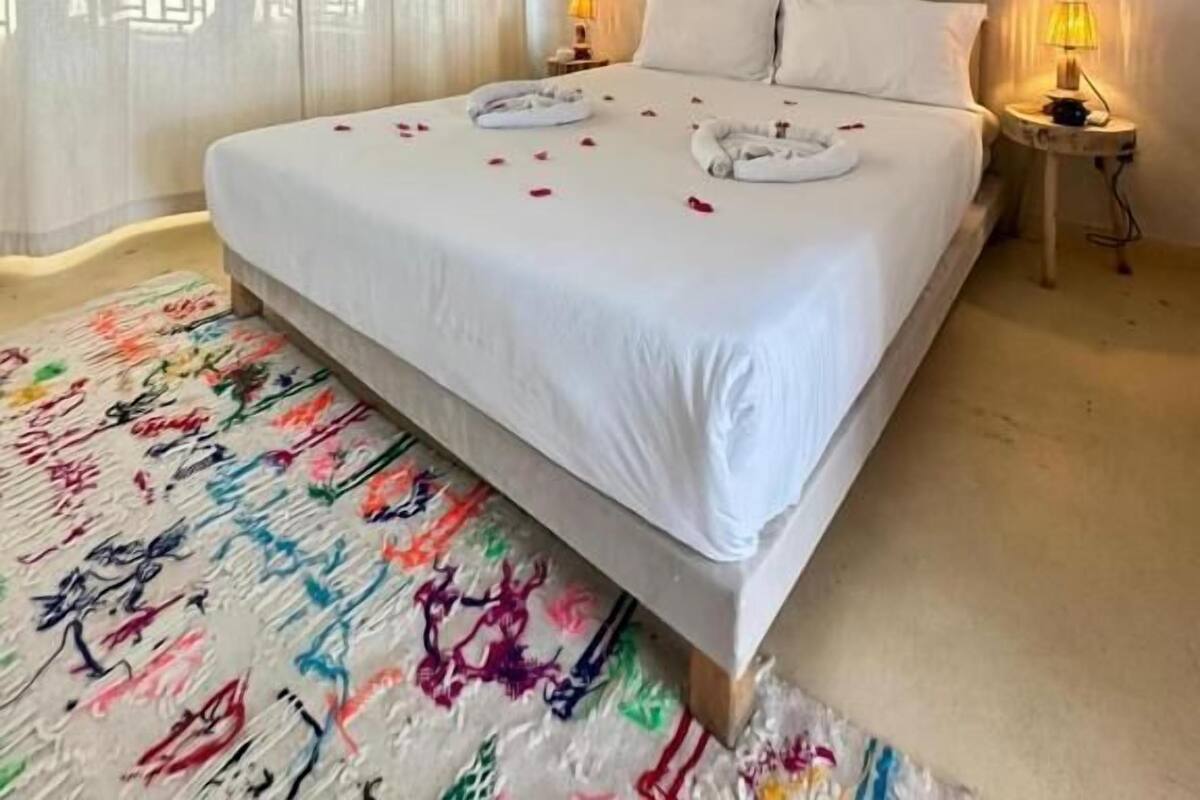 A hotel room with a large bed, two bedside lamps, a ceiling fan, and a window with curtains.