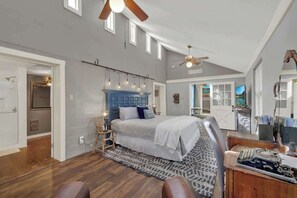 A bedroom with a large bed, a desk with a computer, and a ceiling fan.