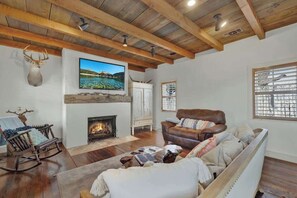 A living room with a fireplace, a television mounted above it, and a deer head decoration on the wall.