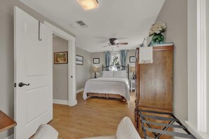 A bedroom with a bed, a wooden wardrobe, a ceiling fan, and a door leading to another room.