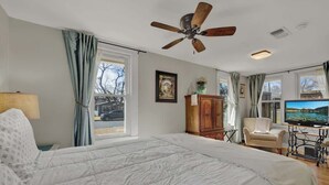 A bedroom with a bed, a ceiling fan, a television, and a view of the outside.