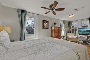 A bedroom with a bed, a ceiling fan, a television, and a view of the outside.